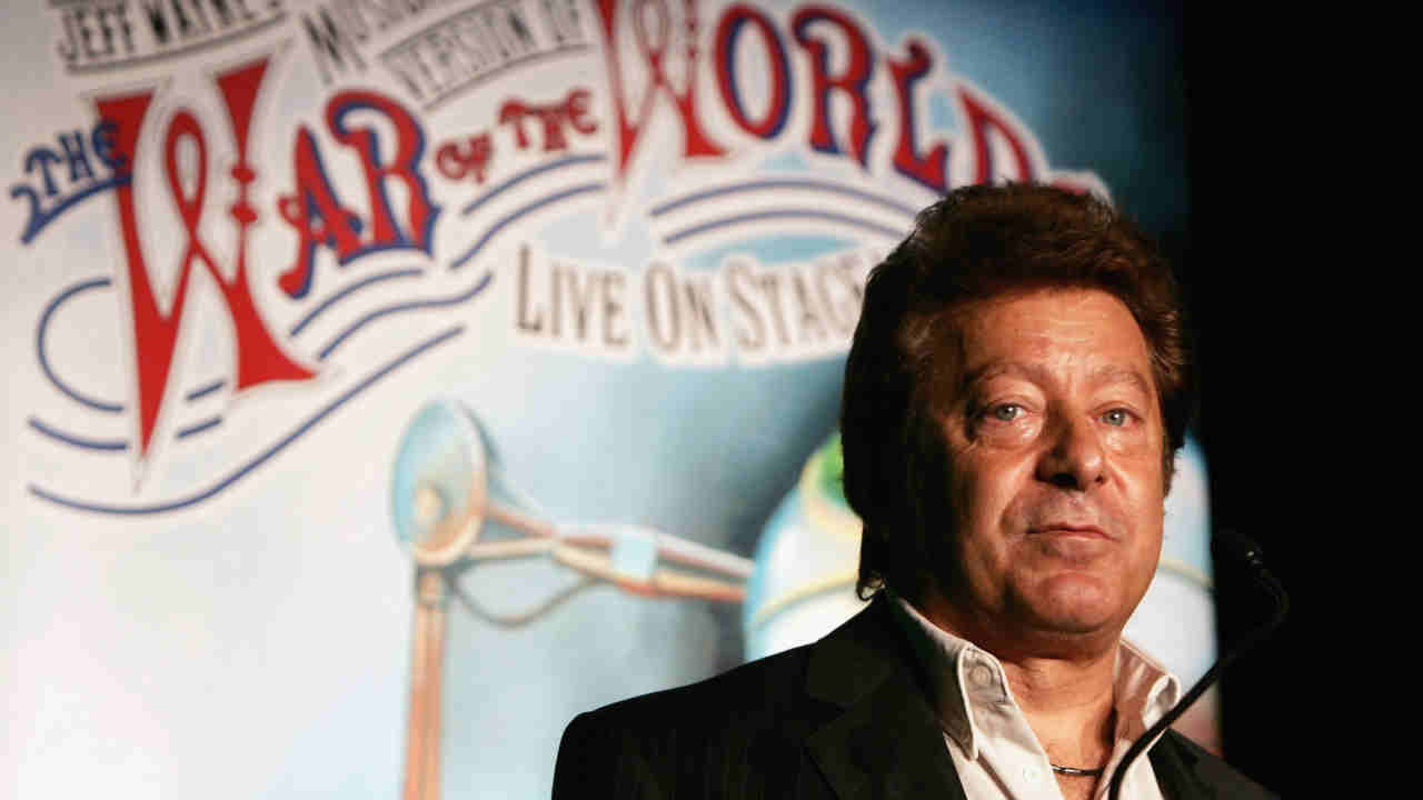 Jeff Wayne posing for a photograph in front of a War Of The World poster in 2007