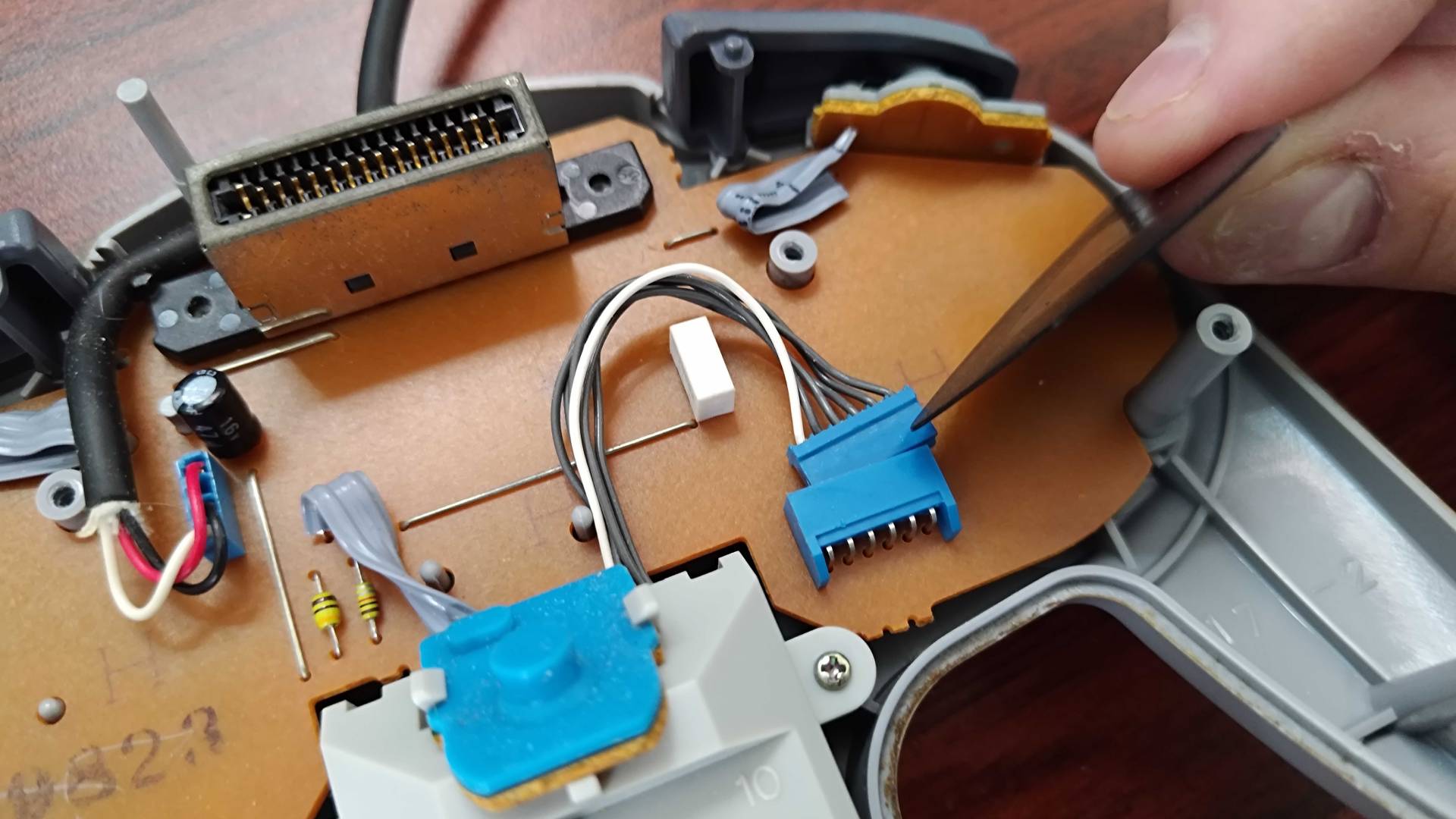 Close up of inside N64 controller with thumbstick in view and hand removing cable from board.