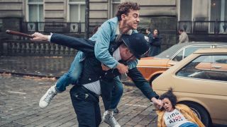 A male character jumps on a policeman as a woman lies on the floor in It's a Sin