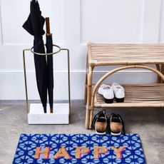 Gold & Marble Umbrella Stand inside hallway with blue doormat that reads 'HAPPY', beside rattan shoe storage