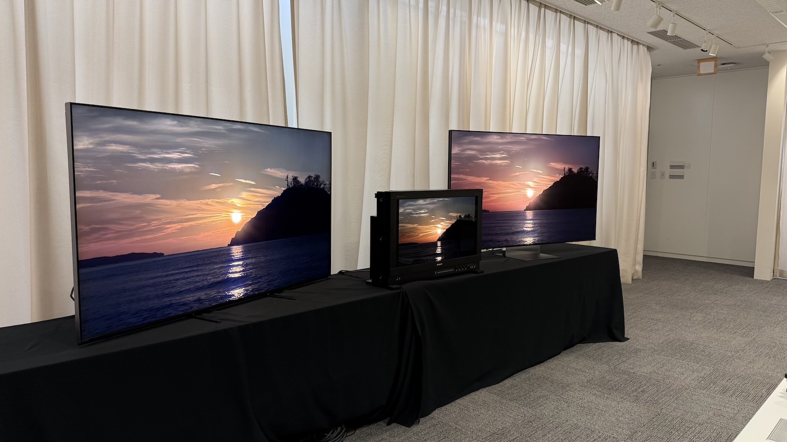 The Sony Bravia 9 II and Bravia 9 TVs, and the Sony BVM-HX3110 mastering monitor, photographed on a black desk, with Sony demo footage on the screens