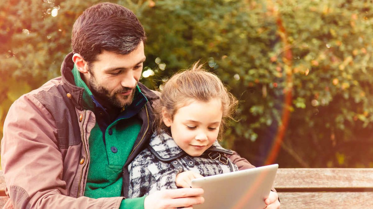 A father reads from a tablet computer with his daughter outdoors