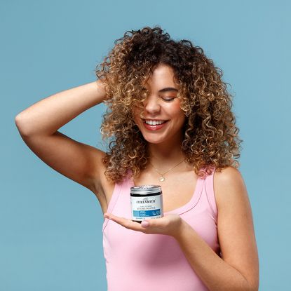 Model scrunching up her hair holding a jar of Curlsmith Styling Souffle