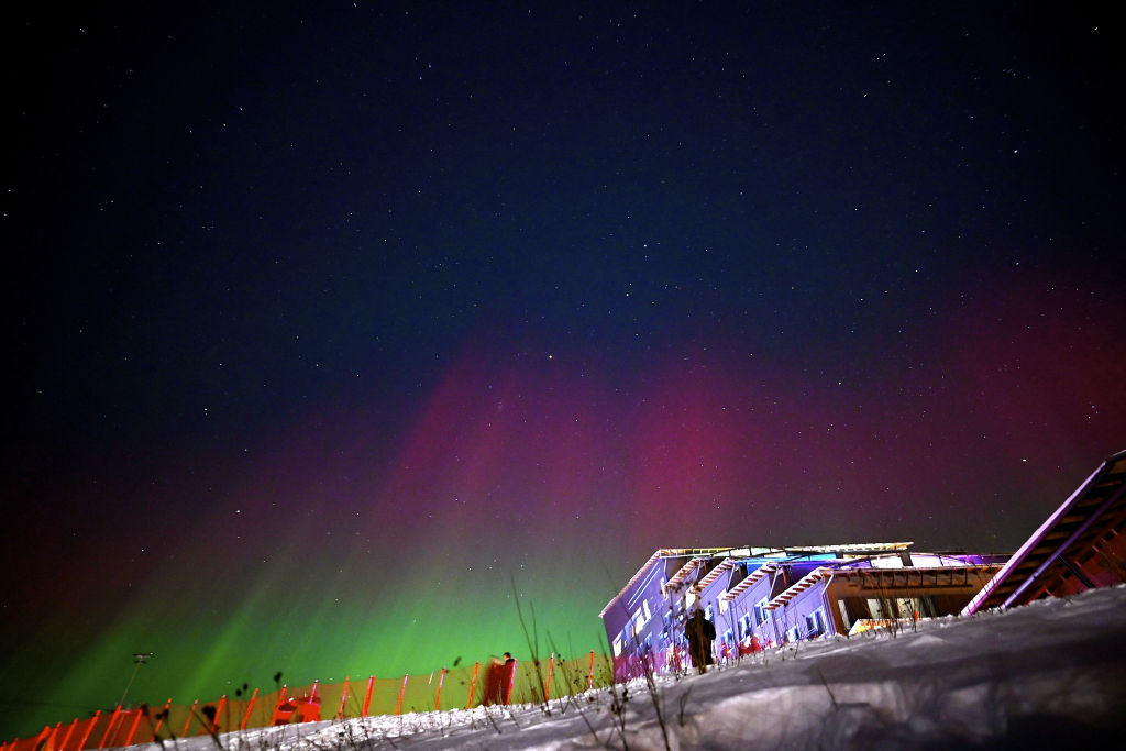 Northern lights over a ski slope fill the sky with red and green northern lights.