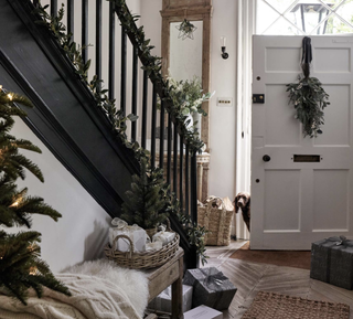 White hallway with a black staircase decorated in Christmas décor with a white open door and presents in the hallway