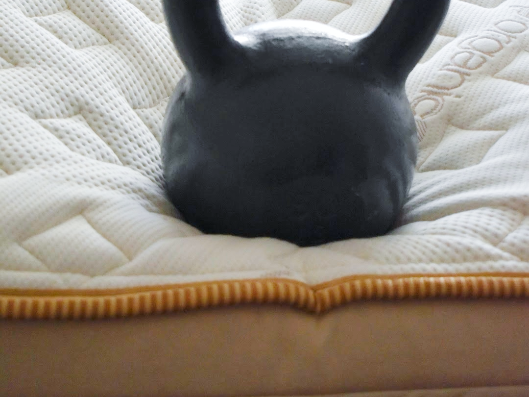 A 50lb kettlebell sits at the edge of the Saatva Memory Foam Hybrid Mattress