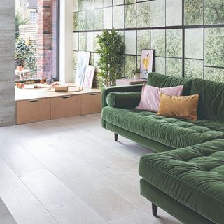 A living room with a kids' play corner and a corner green velvet sofa with contrasting cushions