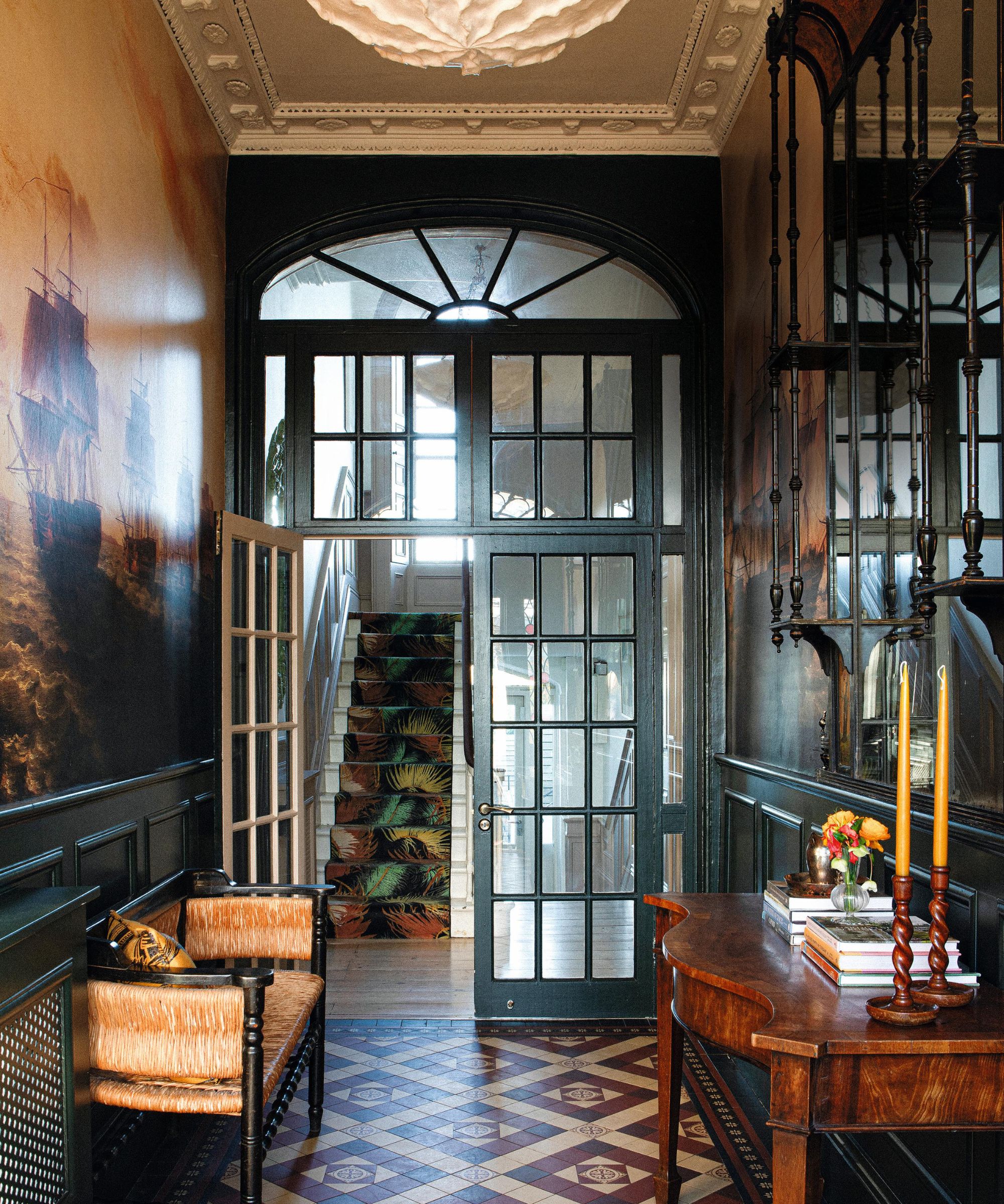 a grand entryway in Dublin with a large glass porch door with arched window, victorian floor tiles and a mural wallpaper with vintage hallway tables