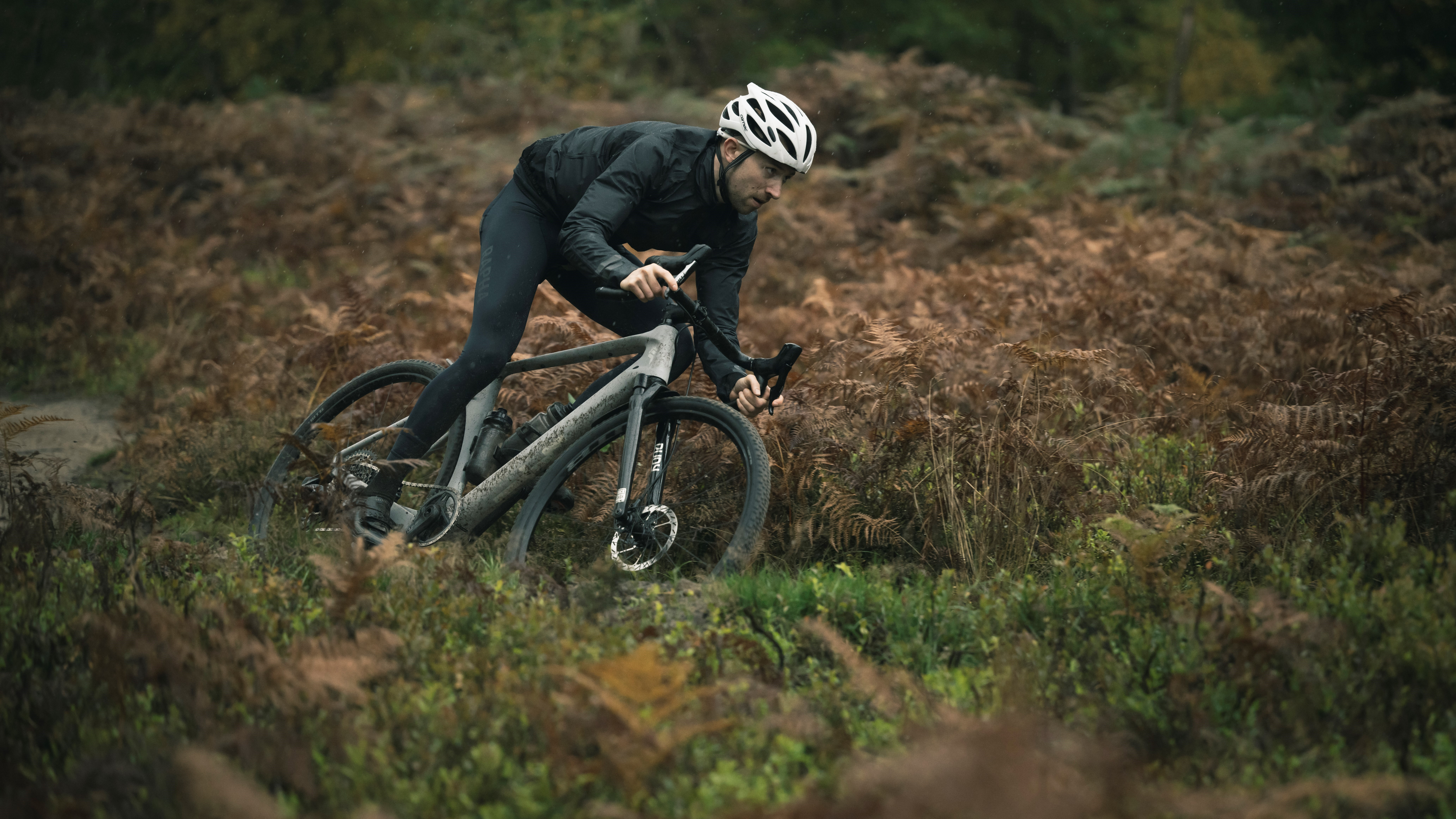 A man in a pair of bibtights riding a gravel bike through a wood