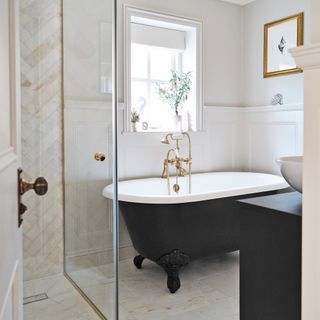 a bathroom with a large freestanding black painted bath tub and shower with white panelling and cream tiles