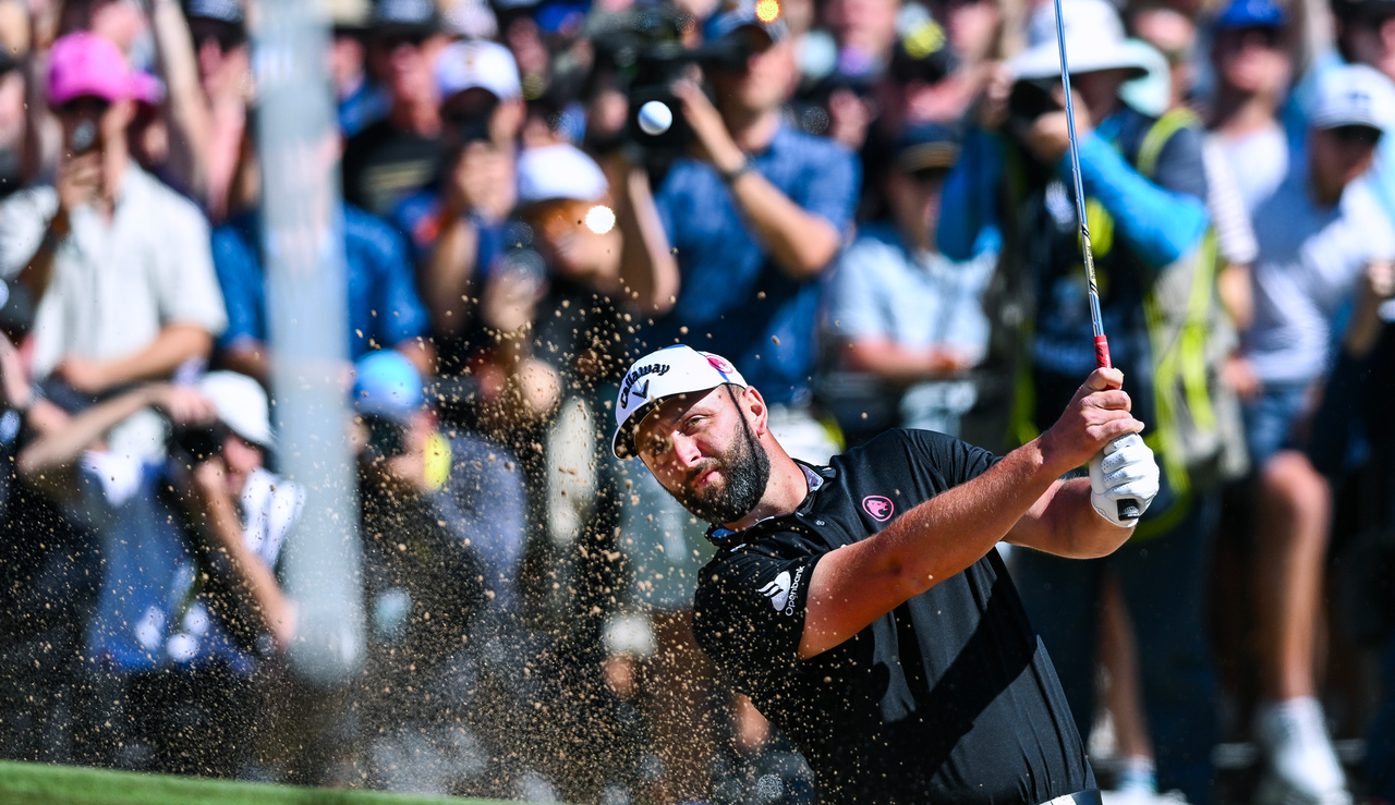 Jon Rahm hits a bunker shot and watches its flight