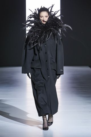 Woman on runway in black Dolce & Gabbana coat with feathers around neck