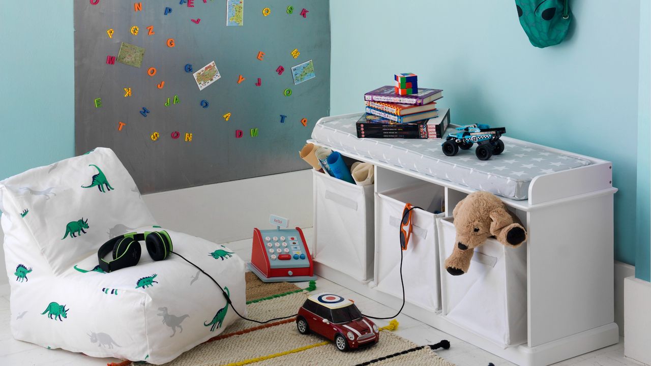 A light blue playroom with a magnetic board, a storage bench and a bean bag