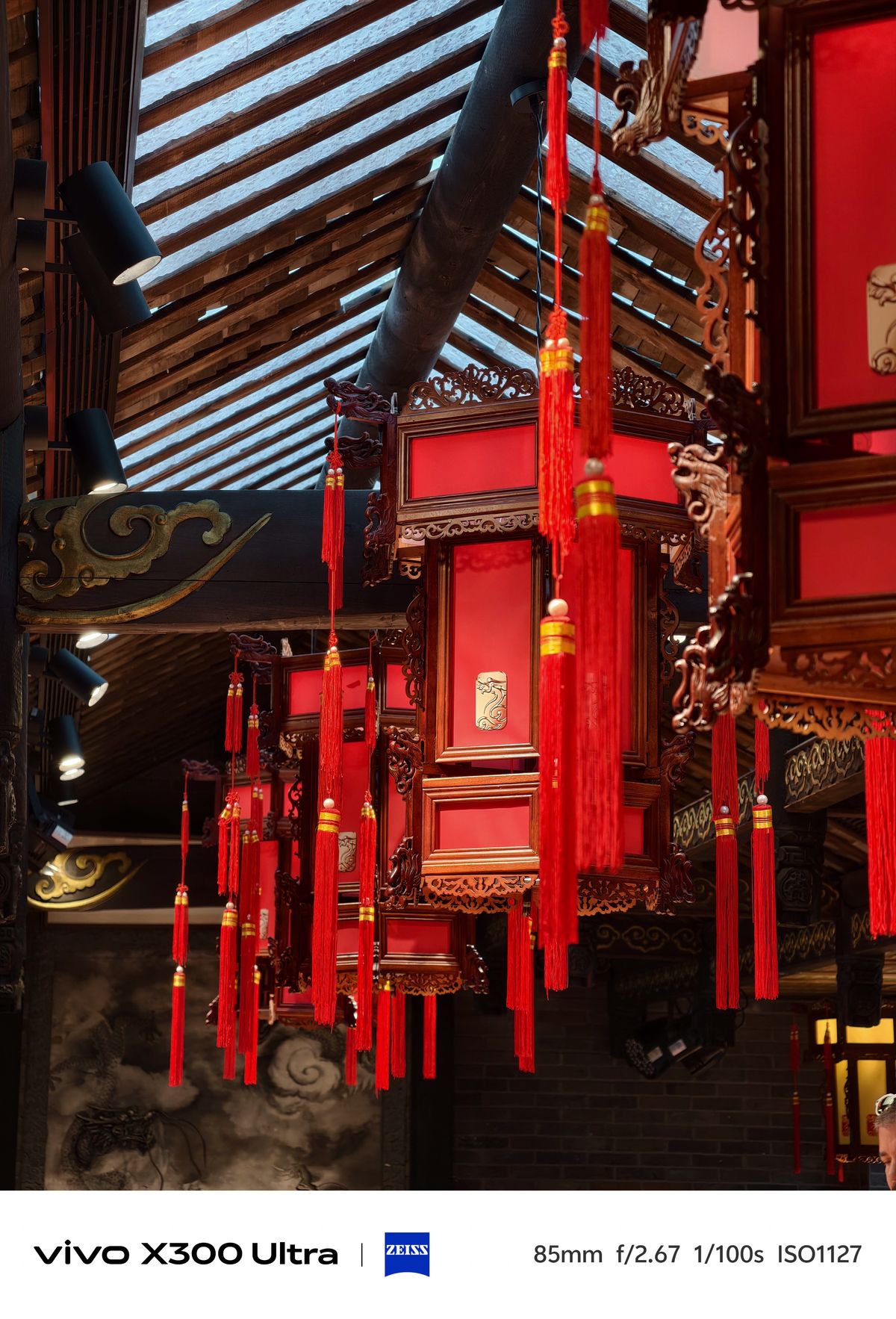 Ornate red wooden lanterns with tassels hanging from a rustic timber roof structure.