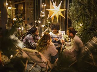 Four people sit around an outdoor table under lights