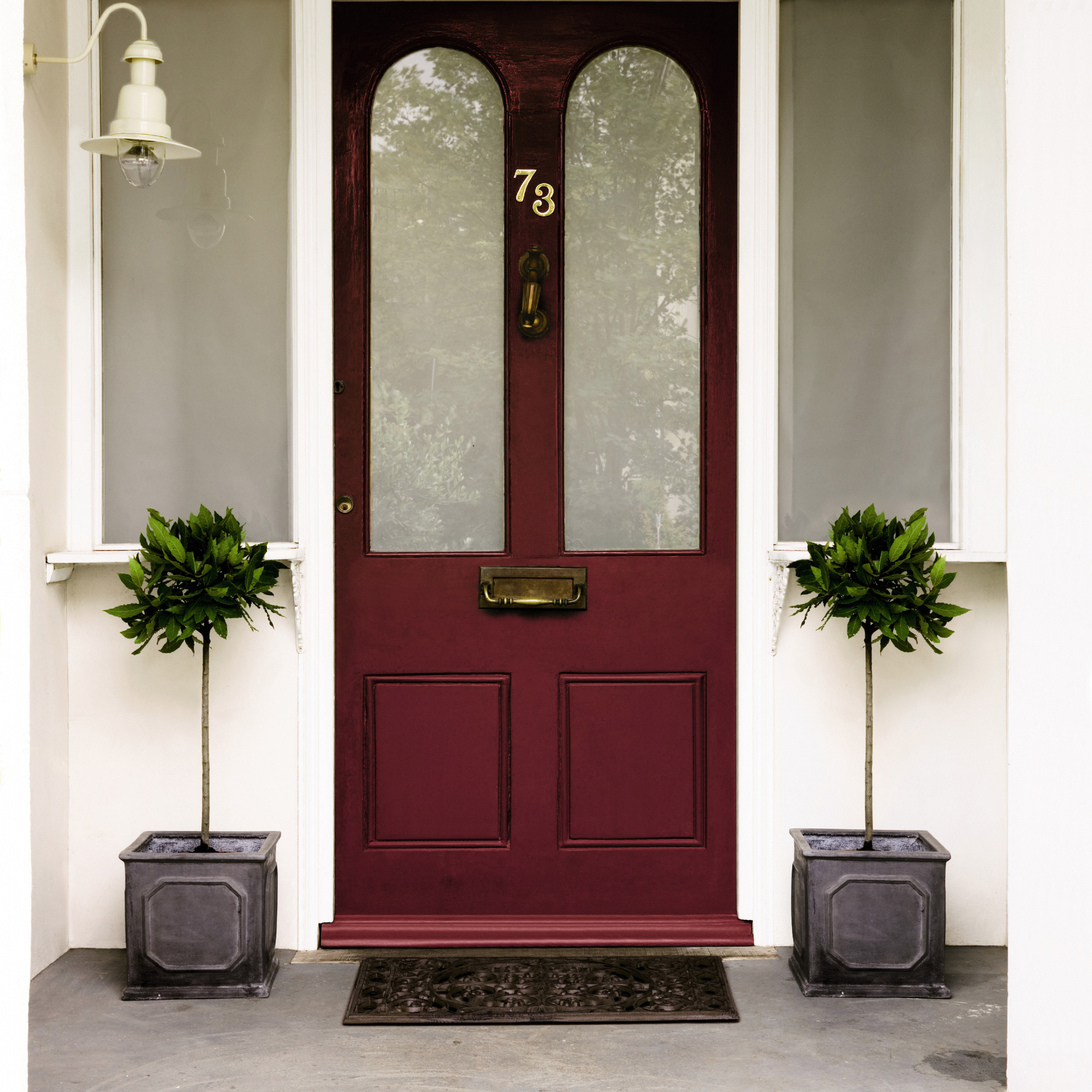 small front porch ideas, maroon front door, pair of bay trees each side, white masonry, enamel wall light, metal door mat
