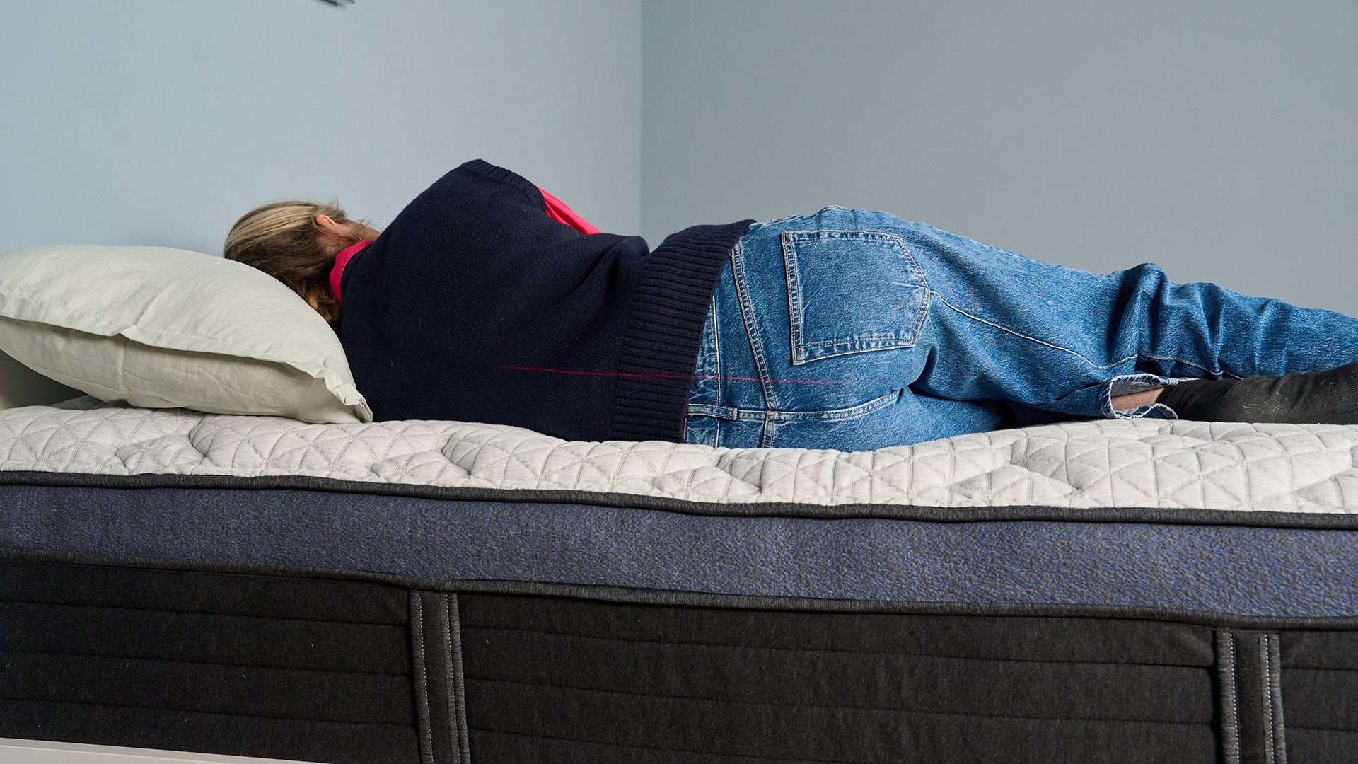 Tom's Guide Sleep Editor Nicola Appleton, dressed in blue jeans and a black top, sleeps on her side on the Helix Midnight Luxe mattress during a pressure relief test.