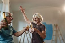 Happy senior couple having fun while toasting with champagne during home renovation process. Focus is on woman.