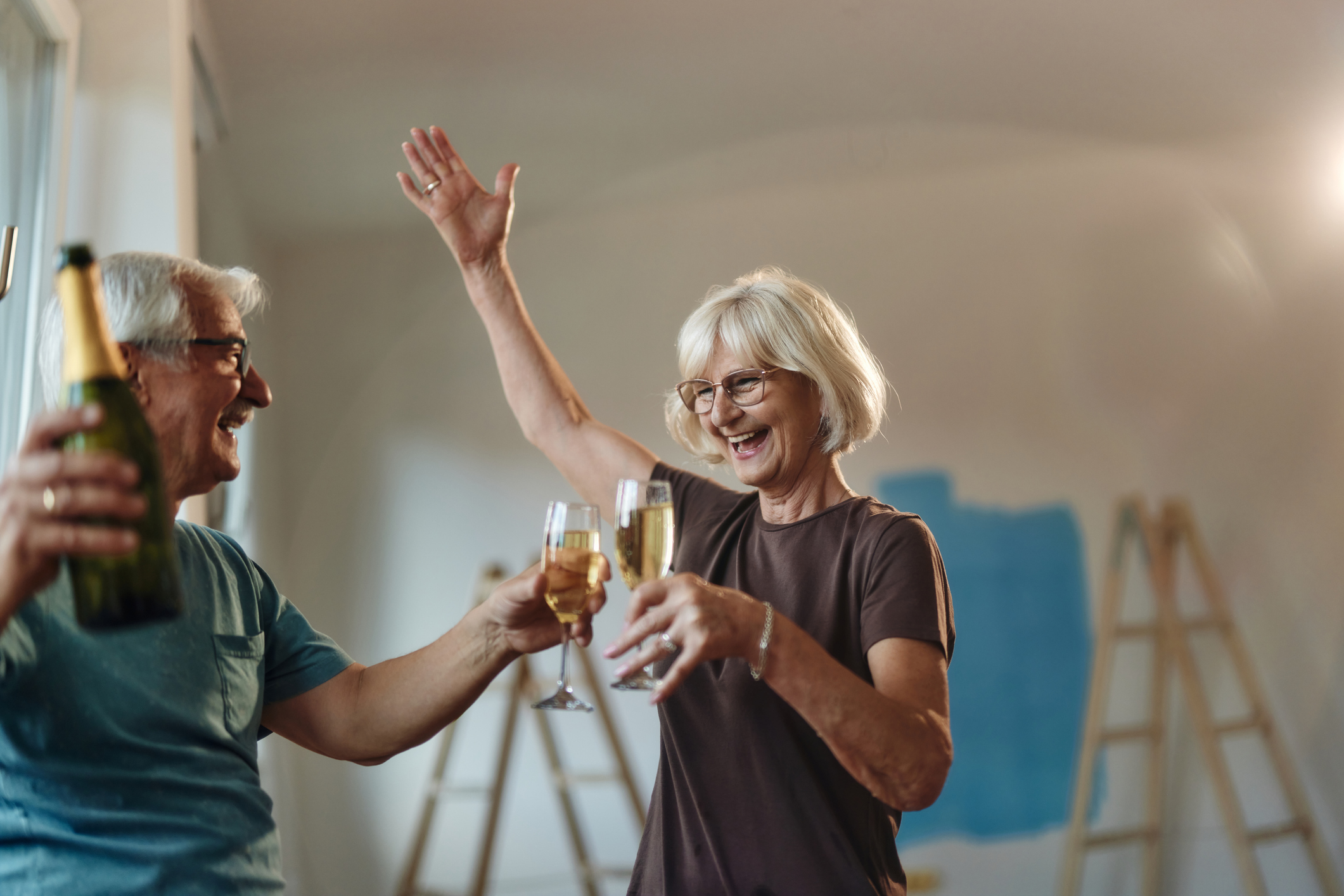 Happy senior couple having fun while toasting with champagne during home renovation process. Focus is on woman.
