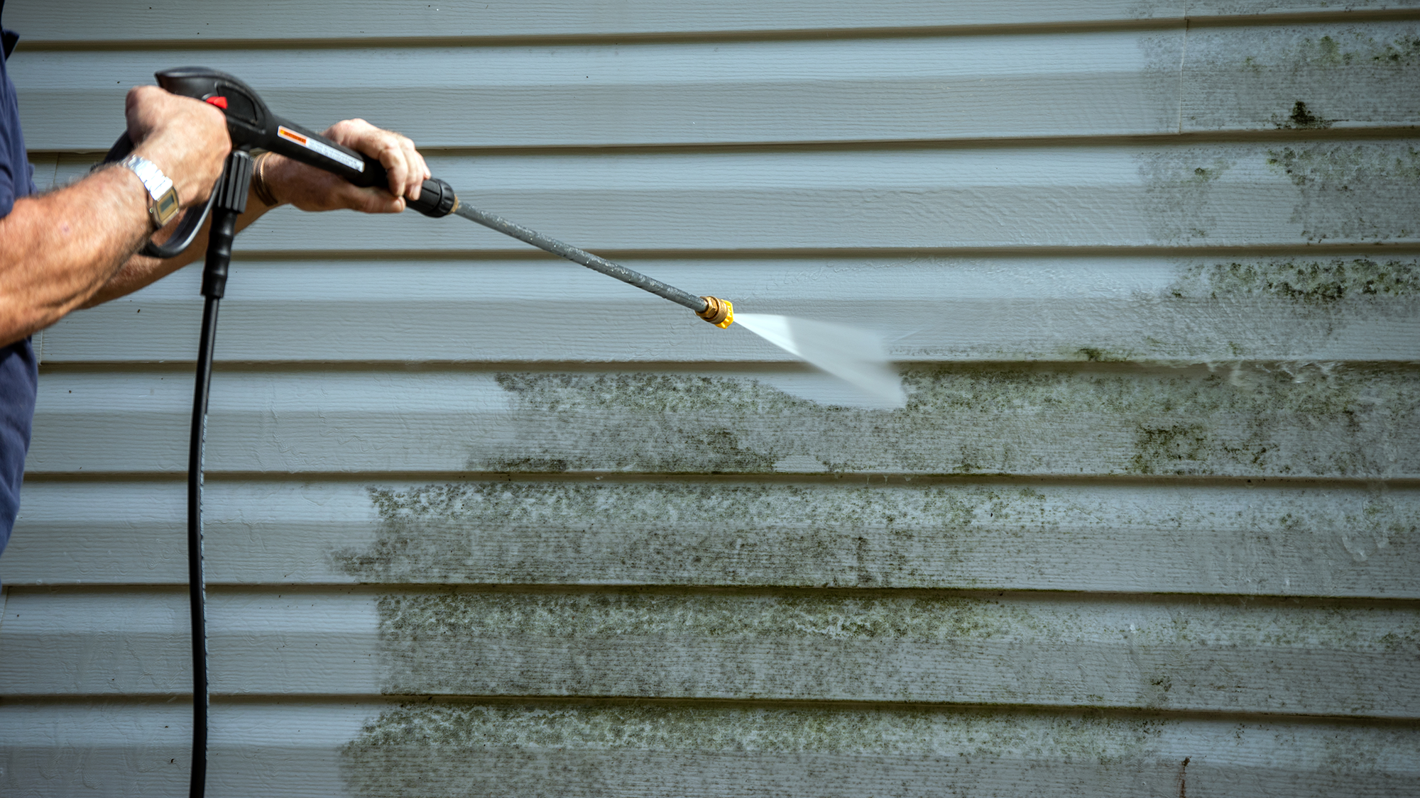Man pressure washing house siding