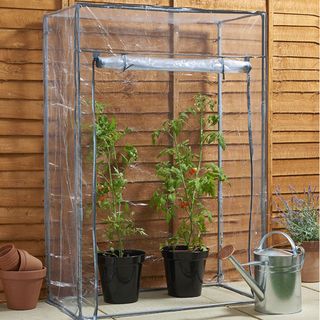 portable plastic greenhouse with plant pots and watering can