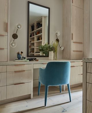 walk in closet with wooden cupboards and drawers and teal velvet chair