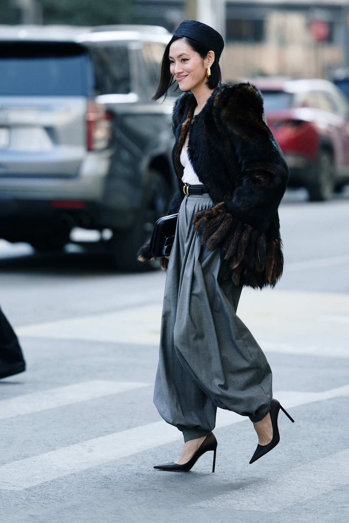 a new york fashion week attendee wearing black pillbox hat, fur coat, grey pants, and black high heels