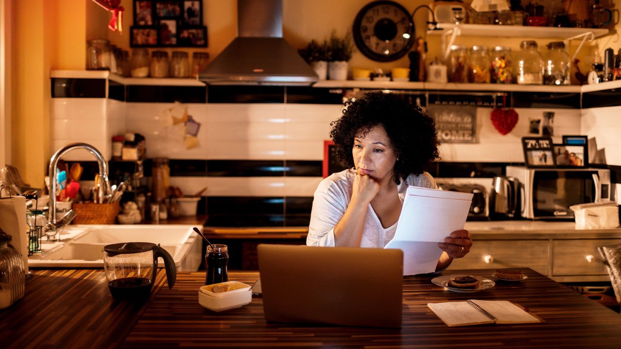 An older woman looks concerned as she looks at her laptop and tax paperwork.