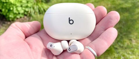 Beats Studio Buds+ in ivory held in hand with charging case
