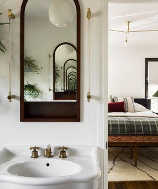 design a home that feels like you, bathroom with brass hardware, large mirror, basin, view into bedroom matching brass hardware, rug, bed, throws and cushions