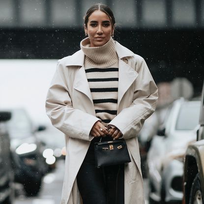 woman wears striped beige sweater with trench coat and black handbag 