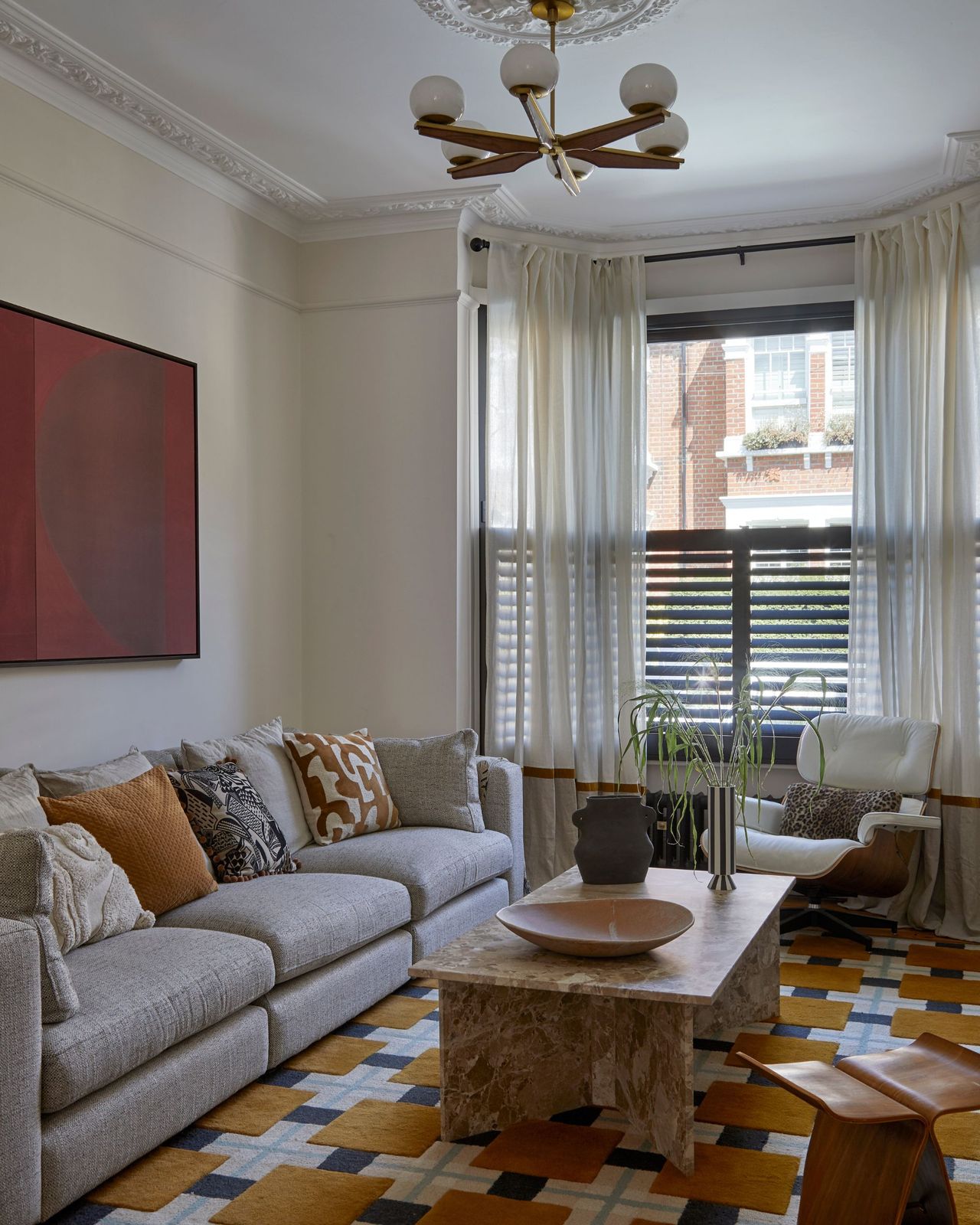 A modern living room with a gray sofa, marble coffee table and large patterned rug with sheer curtains and a pendant ceiling light