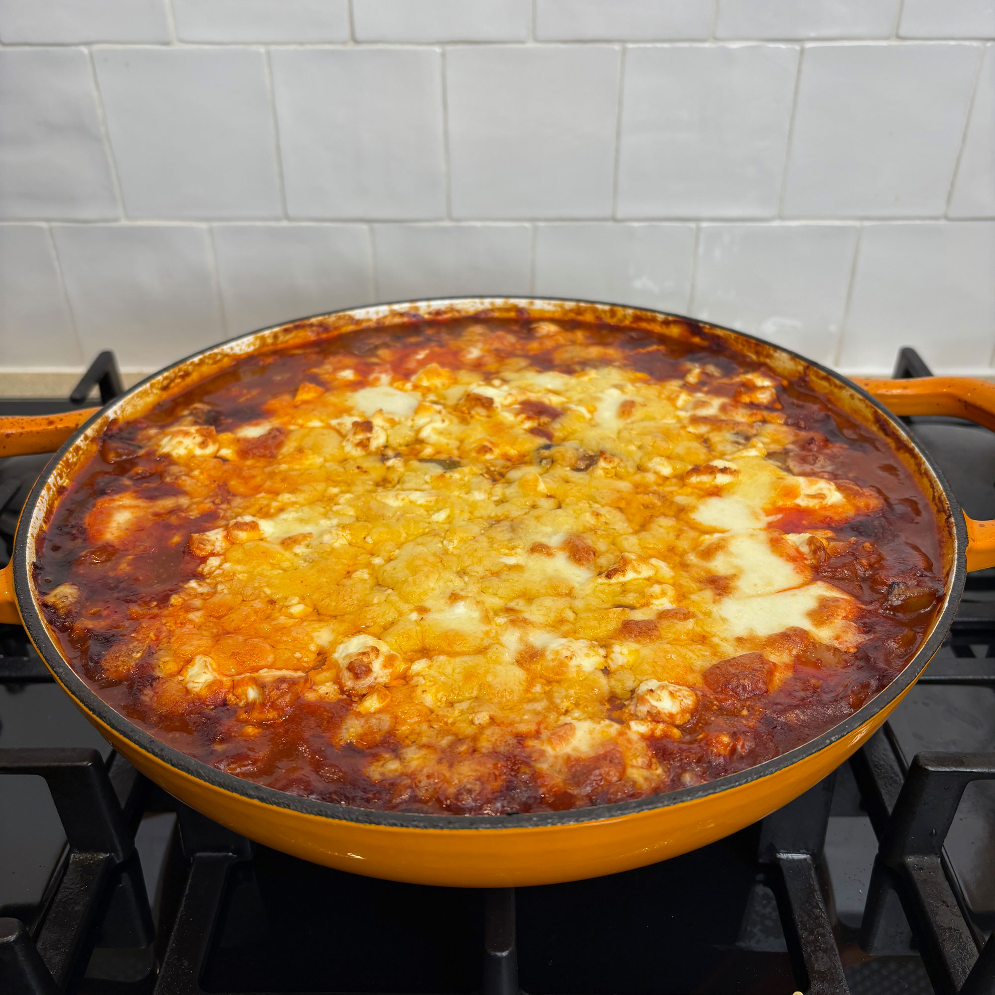 Orange cast iron pan on black hob with baked cheese