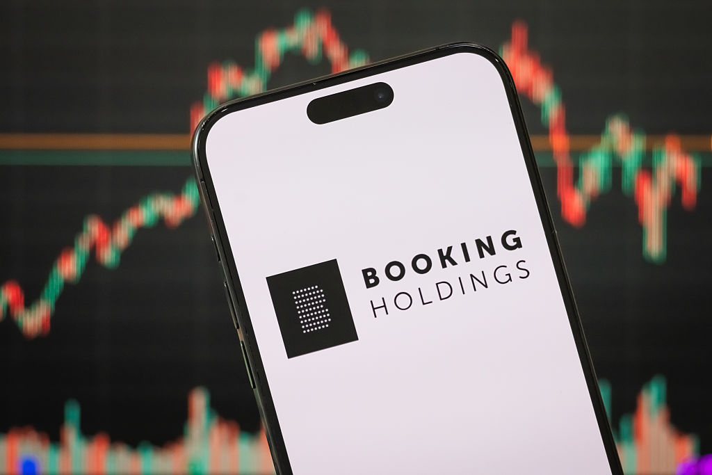 Booking Holdings logo on a smartphone with a blurred stock chart in the background
