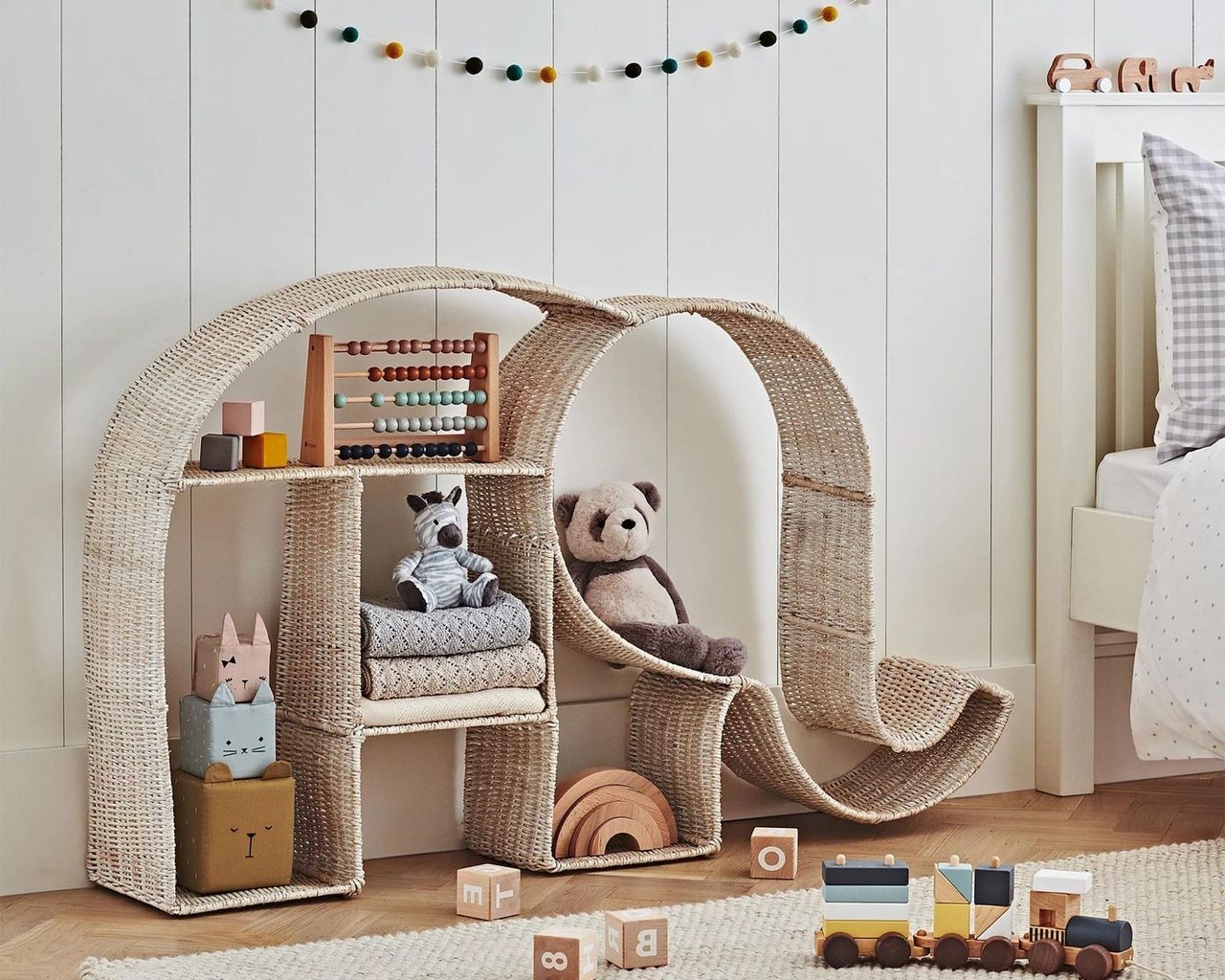 Bamboo elephant shaped bookshelf pushed against the wall in the nursery filled with baby toys including the counter and panda soft toy