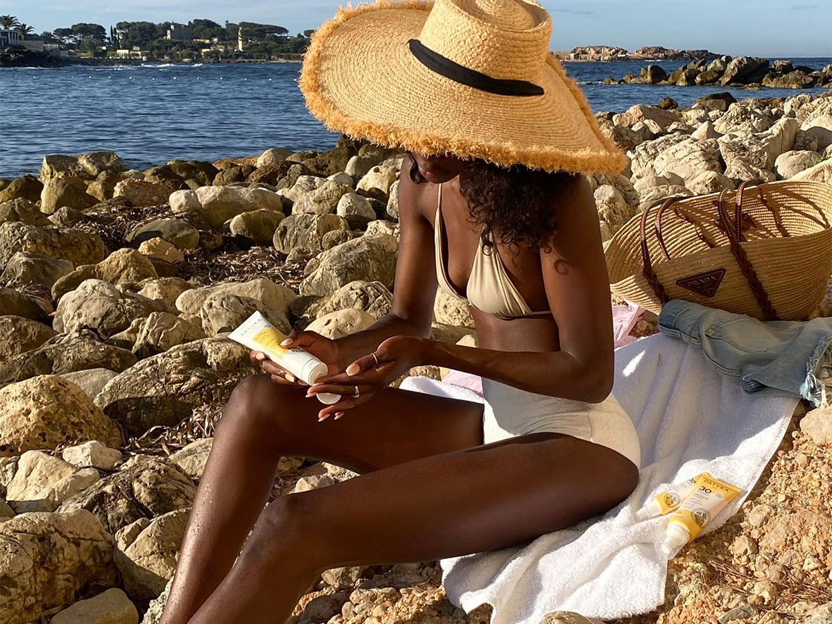 A woman sitting at the beach wearing a white bikini set and a large straw hat.
