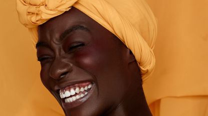 Portrait of smiling young black woman wearing yellow headscarf wearing a cream blusher