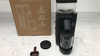 Moccamaster grinder on the countertop with the cardboard box, scoop and lid