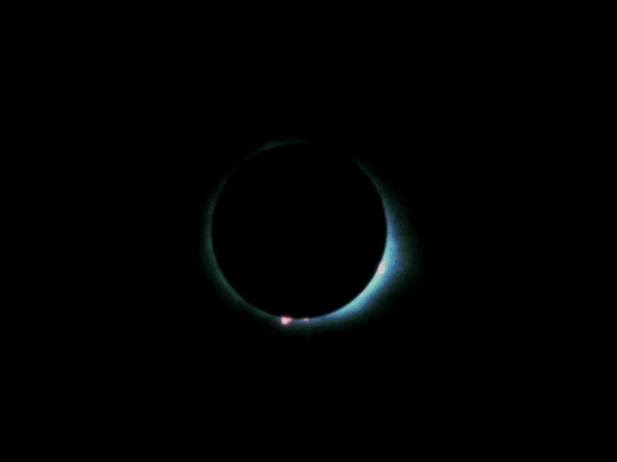 A dark, near-total solar eclipse glows with a faint blue-green corona against a black sky.
