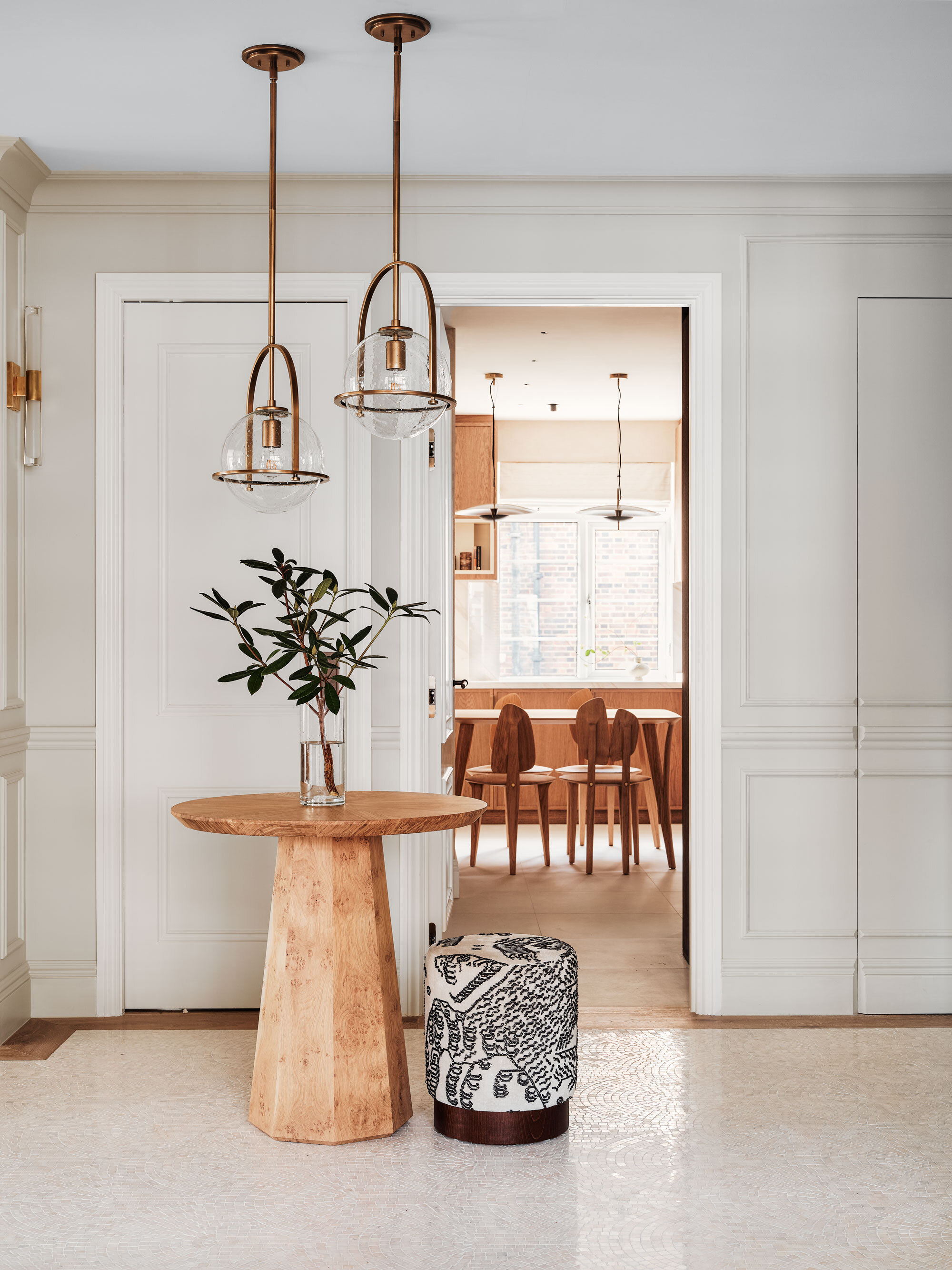 The modern entryway of a renovated London apartment, featuring a natural wood hall table and glass hanging lighting