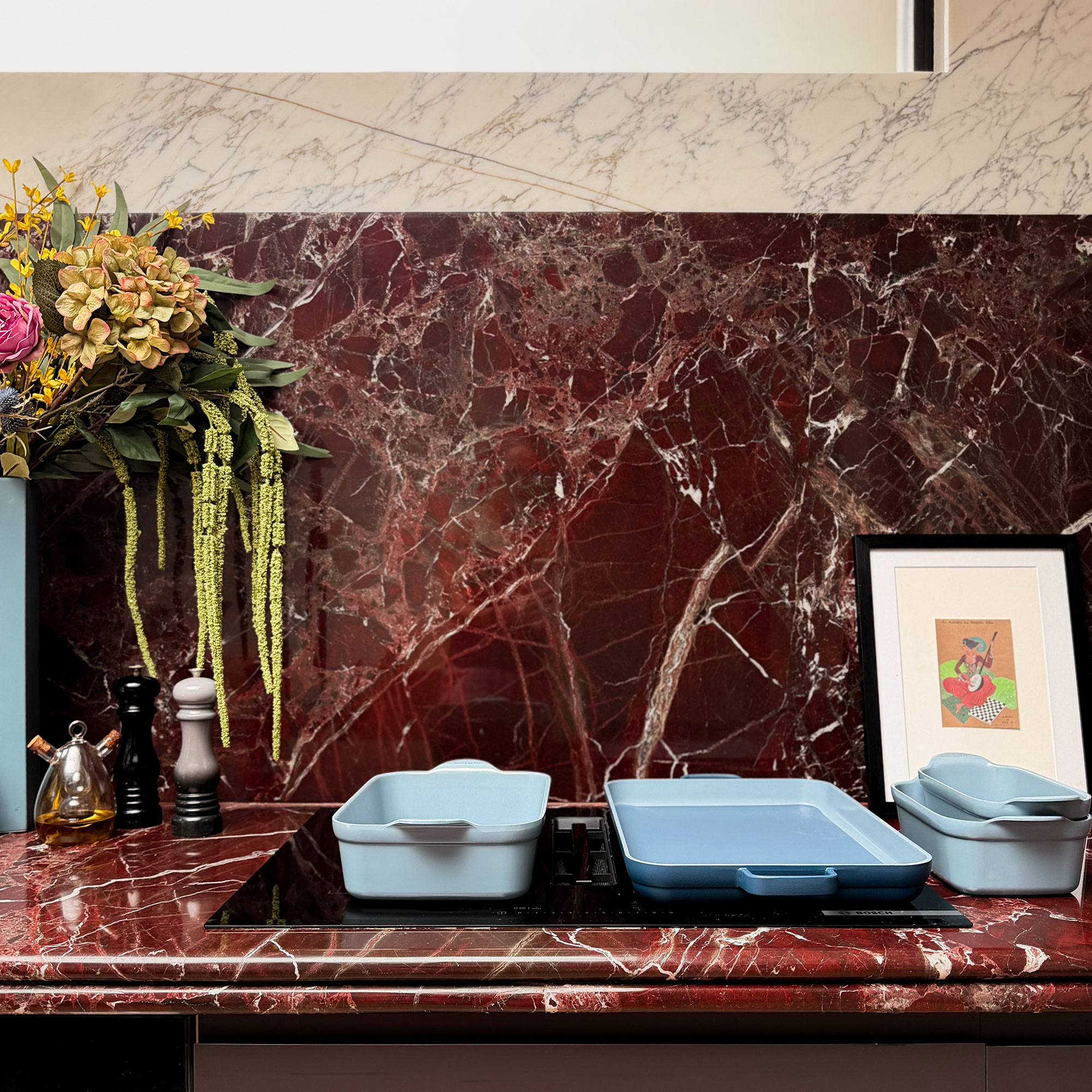 Blue bakeware on hob in kitchen with red marble worktop and red and white marble splashback
