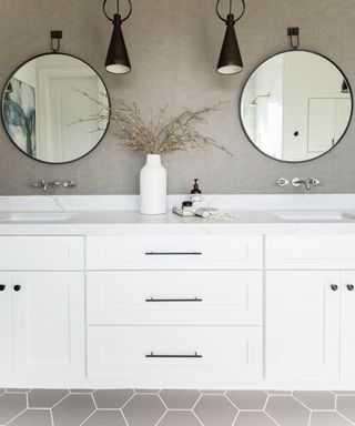 Small gray bathroom with hexagonal gray tiles, pale gray textured wallpaper, black pendants and mirrors, vanity unit with marble countertop,