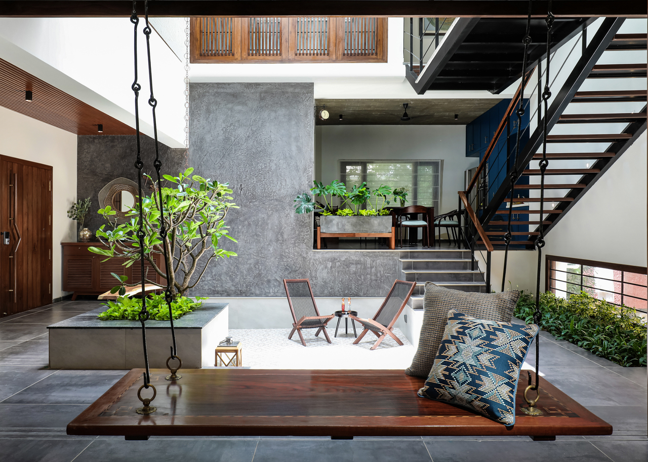 An Indian home with a courtyard by an indoor swing and the stairs with a pair of lounging chairs by an elevated frangipani tree