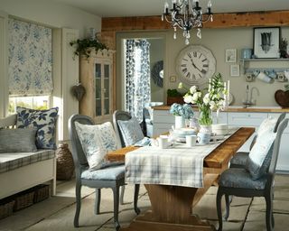 A small dining area in a kitchen with floral window blind, floral cushions and country style dining setup