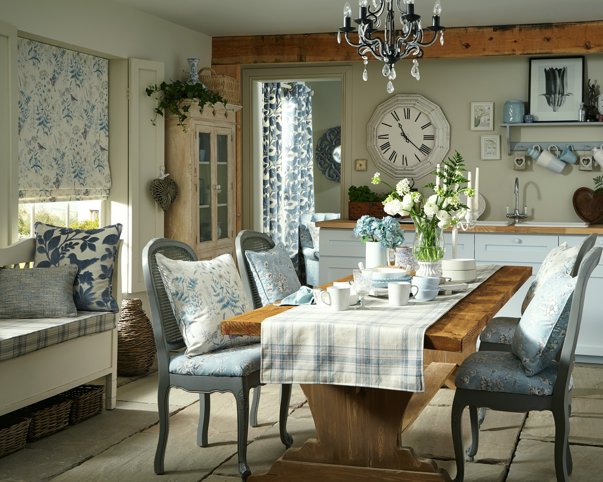 A small dining area in a kitchen with floral window blind, floral cushions and country style dining setup