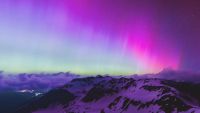 Purple and blue auroras in the night sky above clouds and a mountain