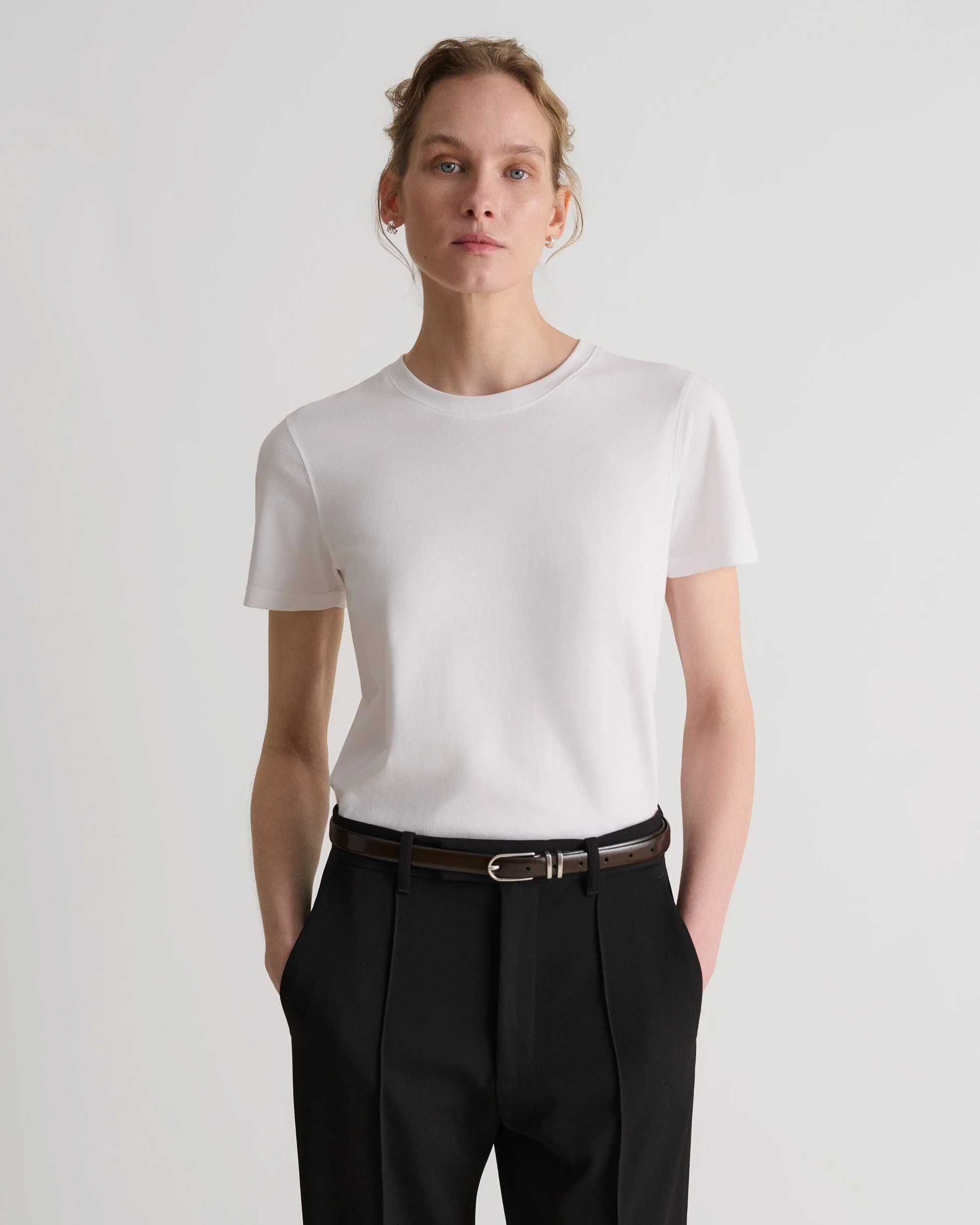 A model wears a white Rise & Fall crew neck t-shirt.