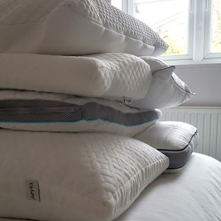 A pile of different types of pillow on a bed in front of a window