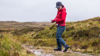 A woman on a muddy trail stopping and looking down at her shoes, which are Salewa Mountain Trainer 2 Mid Gore-Tex Boots.