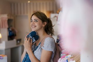 Smiling pregnant woman shopping for baby clothing in a boutique after using old wives tales about pregnancy to guess her baby's gender.